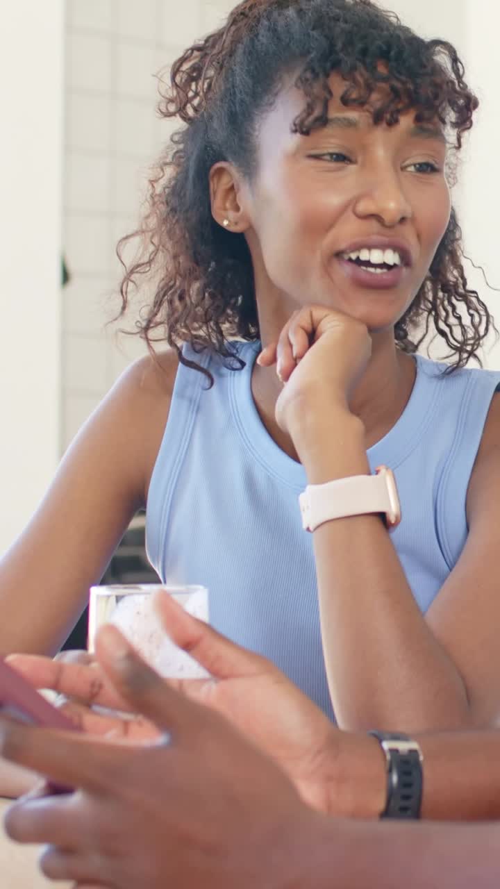 Donna che appoggia il mento sulla mano destra mentre sorride e parla a tavola, con uno smartwatch rosa pallido.