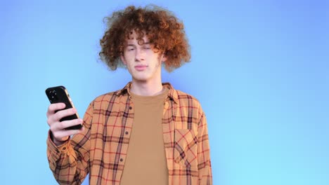 curly guy with a smartphone in his hands on a blue background in the studio curly guy with a smartphone in his hands on a blue background in the studio