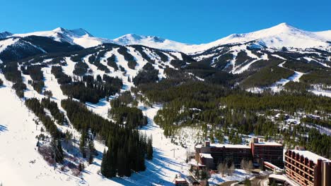 snow-covered ski slope trails at giant winter resort with people skiing and riding chairlifts down mountain through a pine tree forest and snow, aerial drone view