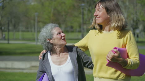 women embracing each other, holding yoga mat in hands, laughing