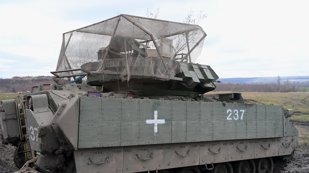 Un veicolo da combattimento della fanteria M2 Bradley di fabbricazione statunitense in servizio ucraino, che mostra la sua duplice identità. La croce medica lo contrassegna per l'evacuazione dei feriti, mentre la 'gabbia anti-drone' lo difende dai droni.