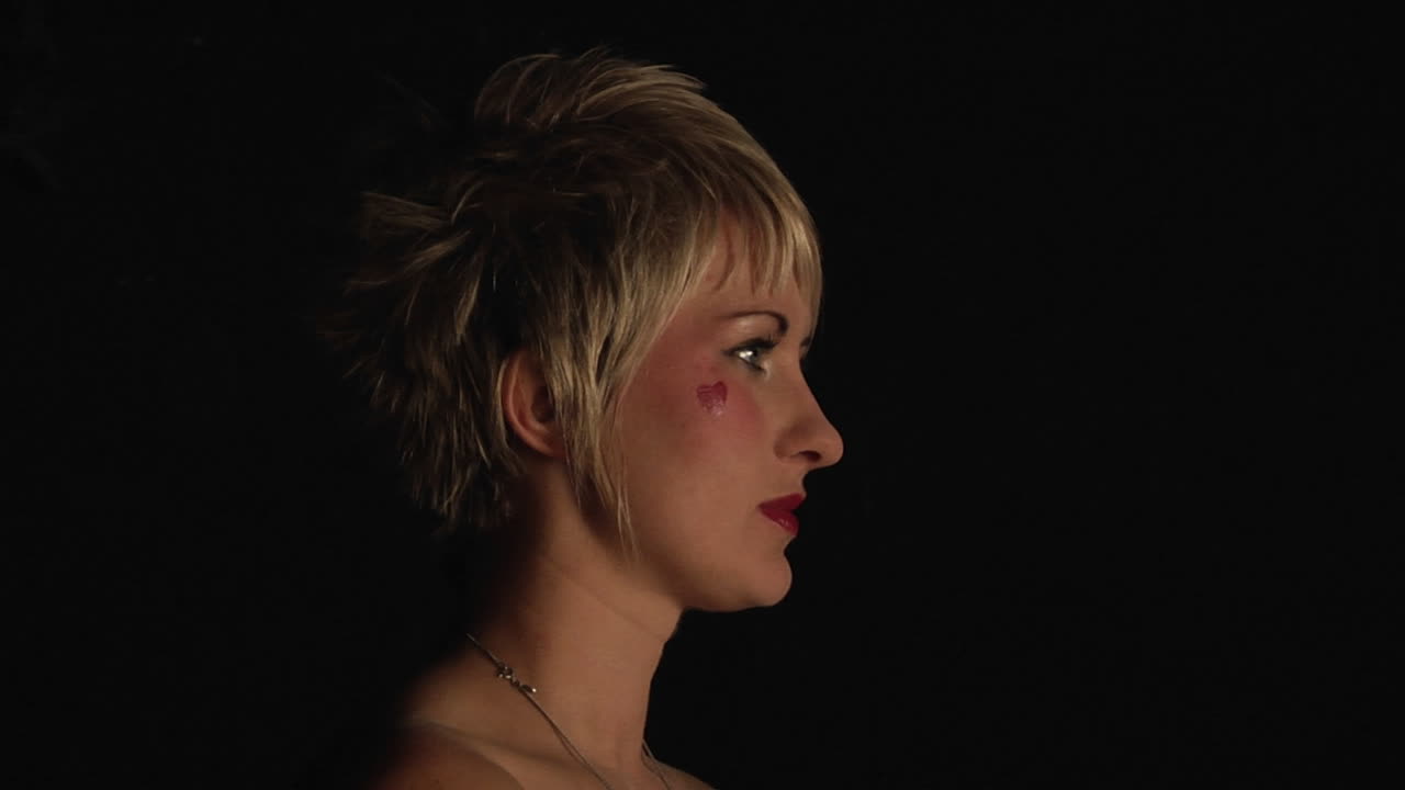 una mujer con un corazón pintado en la mejilla sostiene una máscara blanca en la cara