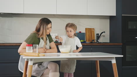 little girl reluctantly mixes whisk of flour with eggs