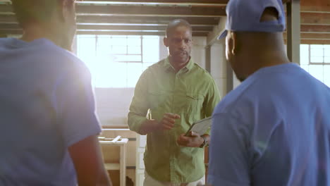 african american supervisor tapping tablet briefing crew confirming cabinet plans in workshop