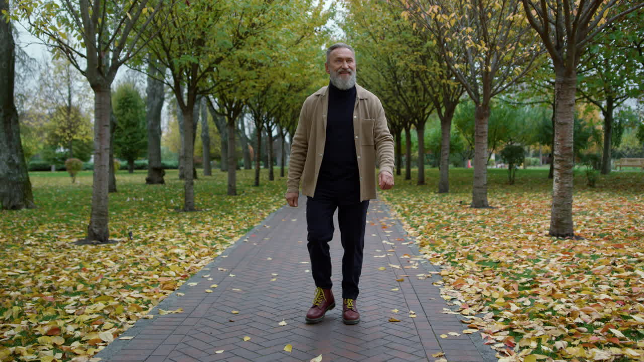Happy confident man walking along alley in park in day time in october.