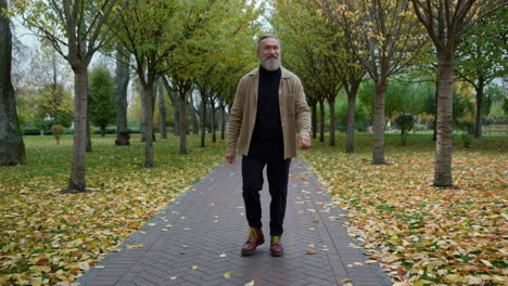 happy confident man walking along alley in park in day time in october.