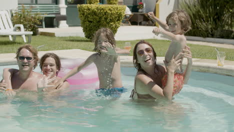 happy family waving at the camera while relaxing and having fun in the swimming pool