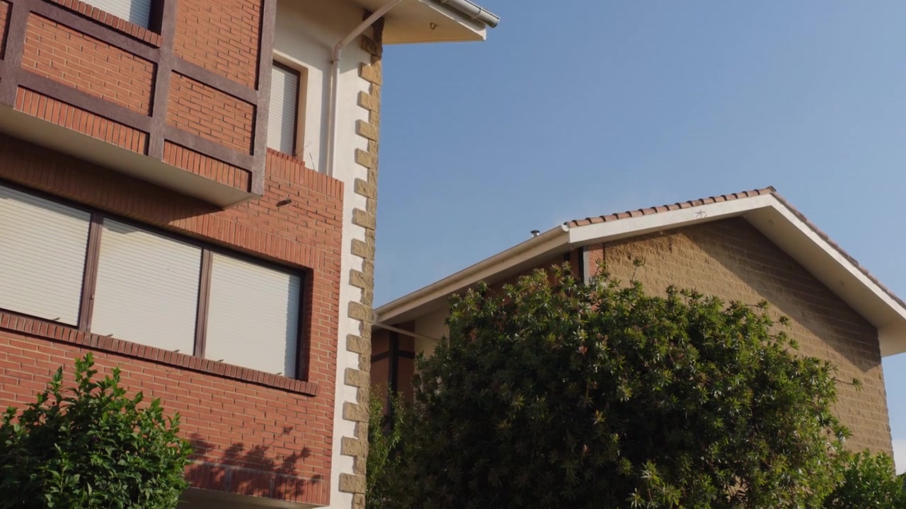 Edifícios residenciais modernos com fachadas de tijolo e telhados de telha sob um céu azul claro, com árvores verdes e luz solar quente