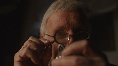 older passionate man evaluates an old silver skull watch in his office at night