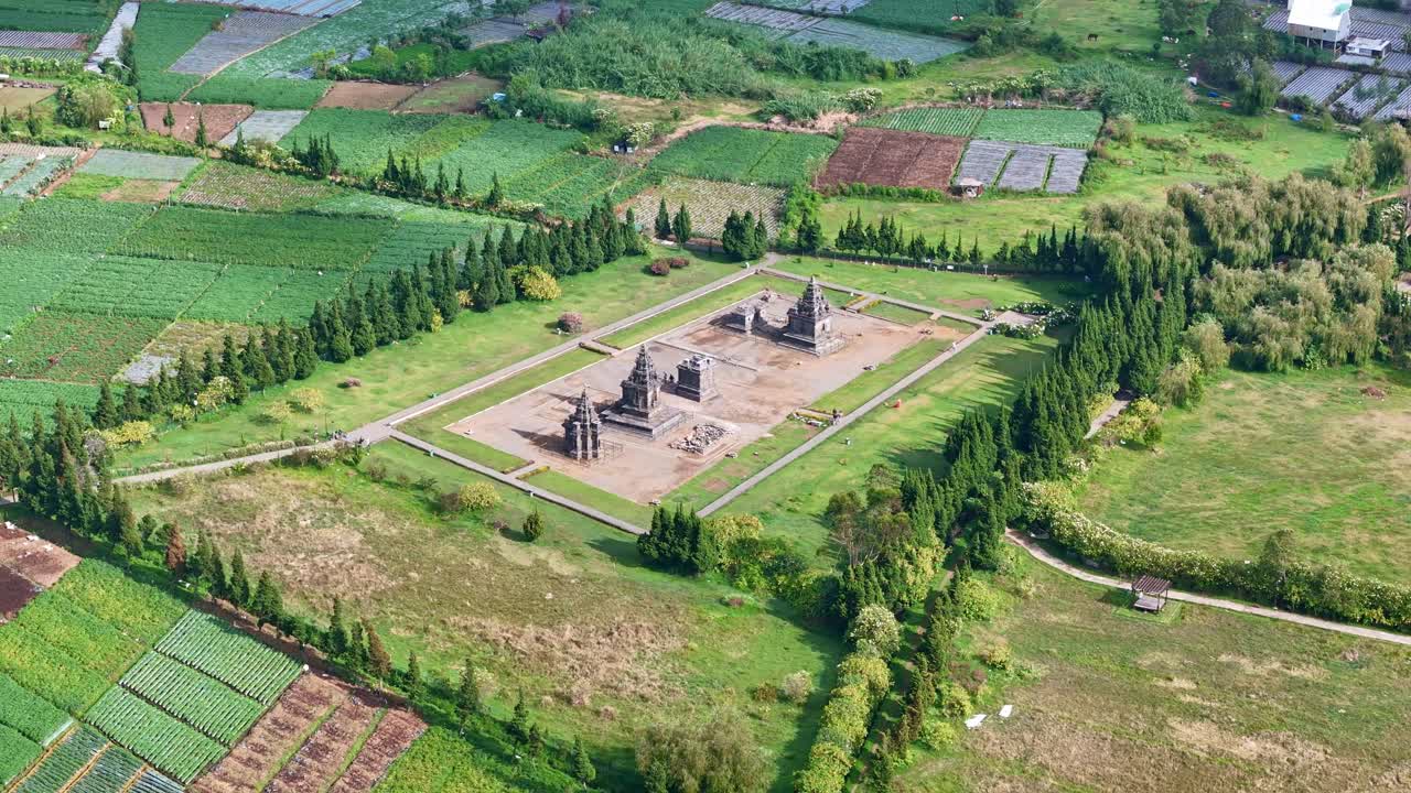 Panoramic aerial view of Arjuna Temple complex in Dieng, Central Java, showing historical stone structures and vast green surroundings