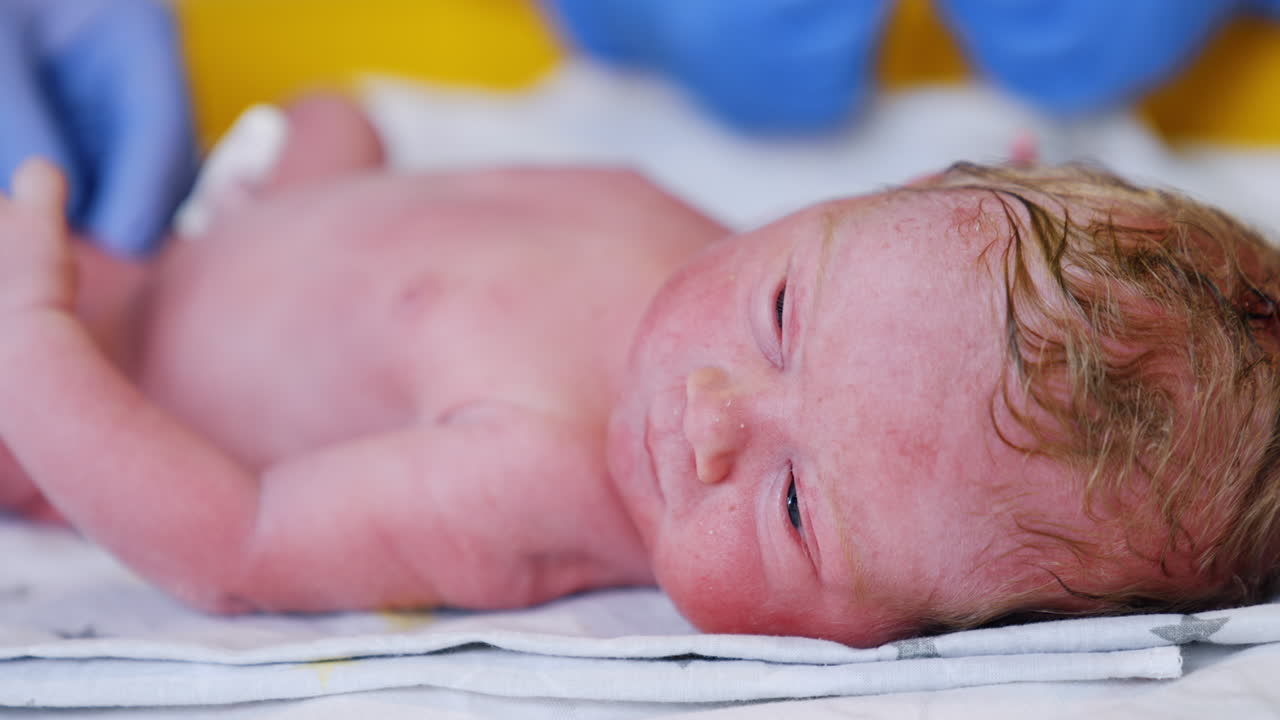 Adorable baby boy with blond hair lies on the table. Calm beautiful child right after birth. Close up.