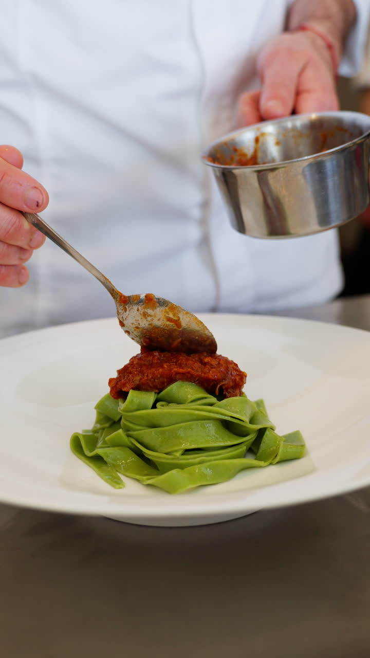 Kok anretter grøn pasta med rød sauce i et professionelt køkken