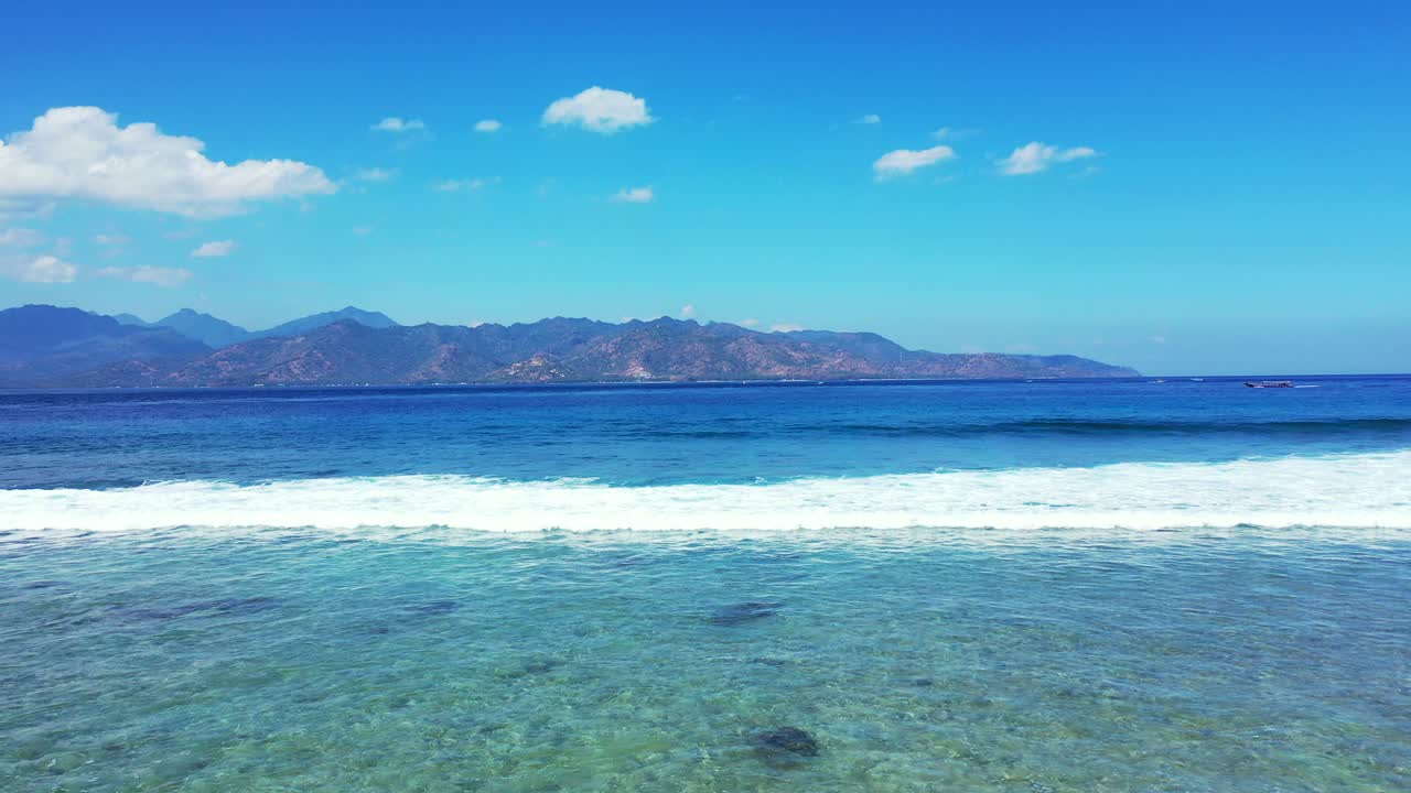 White waves of deep blue sea foaming over rocks and coral reefs on shore with calm shallow water on a bright blue sky background in Malaysia