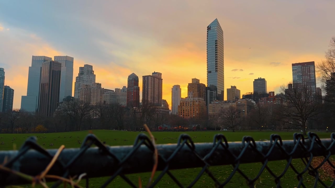 Céu vibrante ao pôr do sol sobre o horizonte de Nova York e uma cerca. Vista da hora dourada dos arranha-céus de Midtown Manhattan atrás de uma cerca de arame metálica no Central Park.