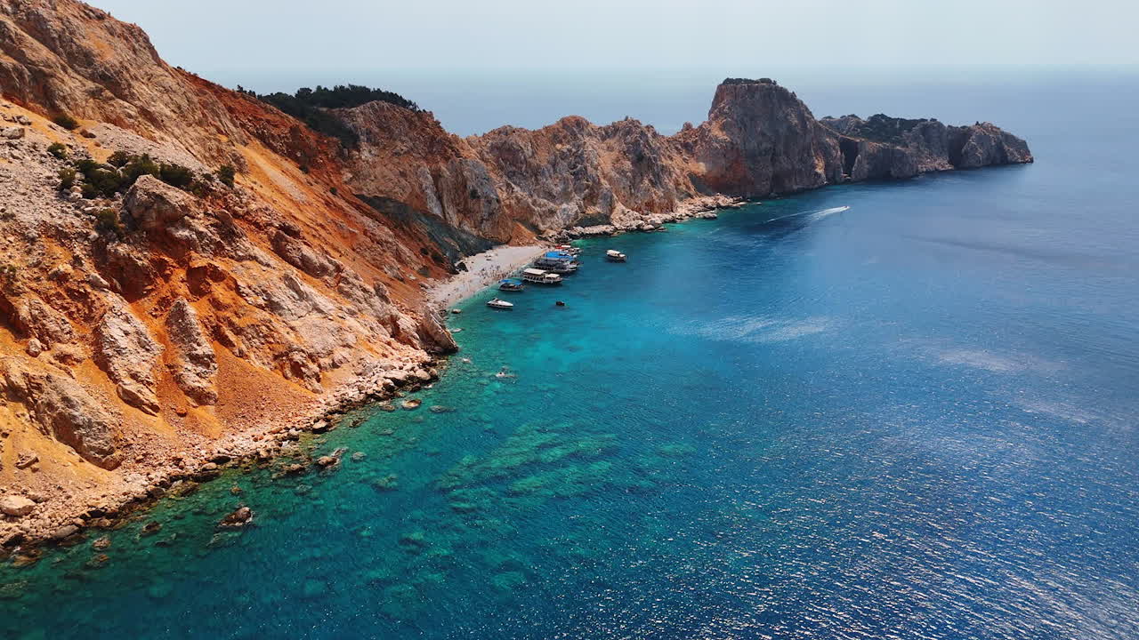 Cliffs meet blue sea in summer. A bright summer day at a stunning coastline with rugged cliffs and boats in turquoise waters