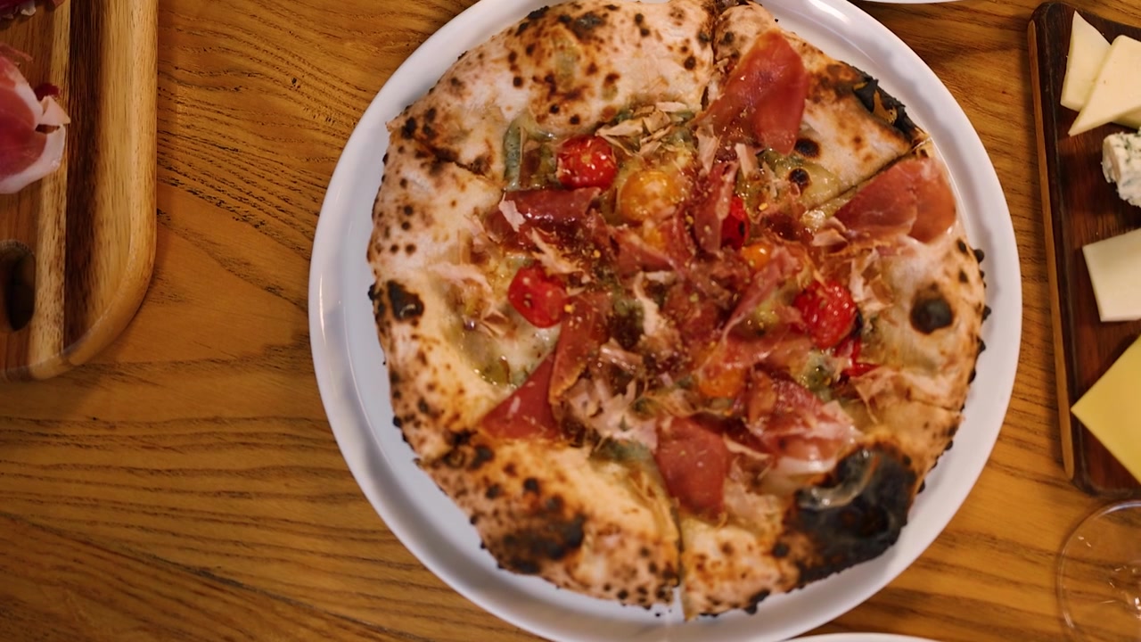 Una ripresa dall'alto mostra pizze gourmet cotte nel forno a legna, taglieri di formaggi e bevande su un tavolo rustico
