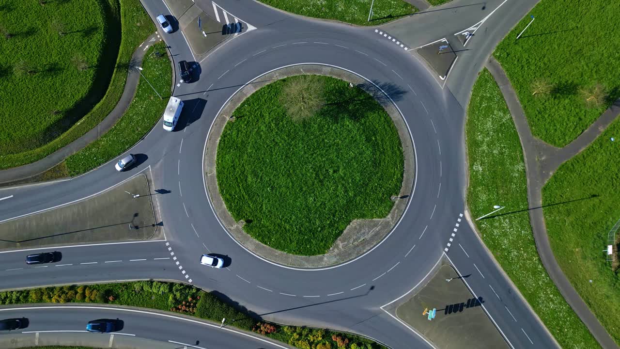 Cars driving on roundabout with green grass center, transportation, infrastructure and road network. Aerial drone top-down descending