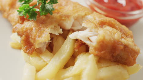 video close up of fish and chips with parsley and bowl of ketchup dip