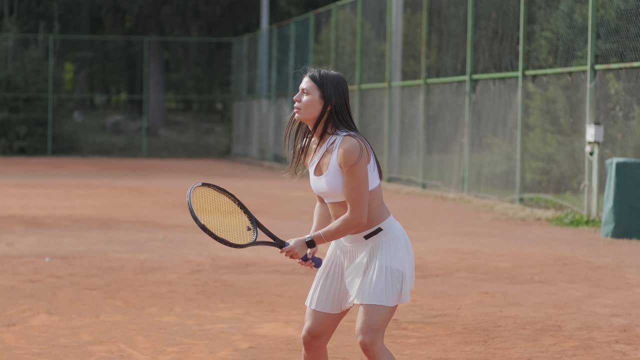 코치와 함께 야외 코트에서 테니스를 연습하는 젊은 여성. 코치는 선수가 그녀의 기술에 대해 일하면서, 운동 훈련 세션에서 그녀의 스트로크를 완성하는 동안 지침을 제공합니다.