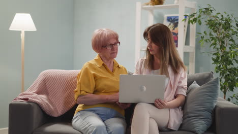 social worker teaches senior lady to use laptop at home