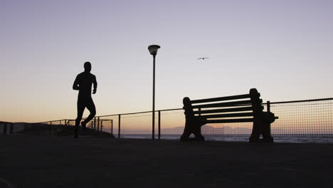 Hombre-Afroamericano-Haciendo-Ejercicio-Al-Aire-Libre,-Corriendo-Junto-Al-Mar-Por-La-Noche