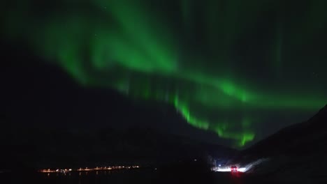 un automóvil conduciendo junto a un fiordo bajo la aurora boreal filmado en tiempo real en la isla de kvaløya, a las afueras de tromsø, en el norte de noruega.