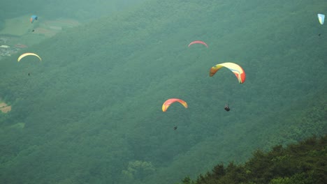 group of paragliders flying around in the air on green mountains background