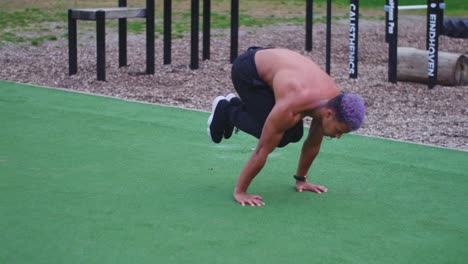 gimbal dolly shot around a shirtless muscular guy who holds a tucked planche as exercise in an outdoor calisthenics sports park