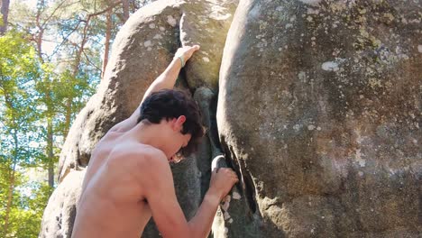 close up of shirtless teenage boy climbing up crag boulder in fontainebleau