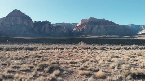 Aerial-drone-shot-of-Red-Rock-Scenic-Highway-with-mountains-in-the-background