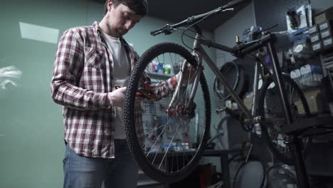 a male bicycle mechanic aligns the tension spokes of a bicycle wheel with a special tool at the workplace in the workshop of a bicycle shop. bicycle maintenance and service. wheel rim alignment tool.