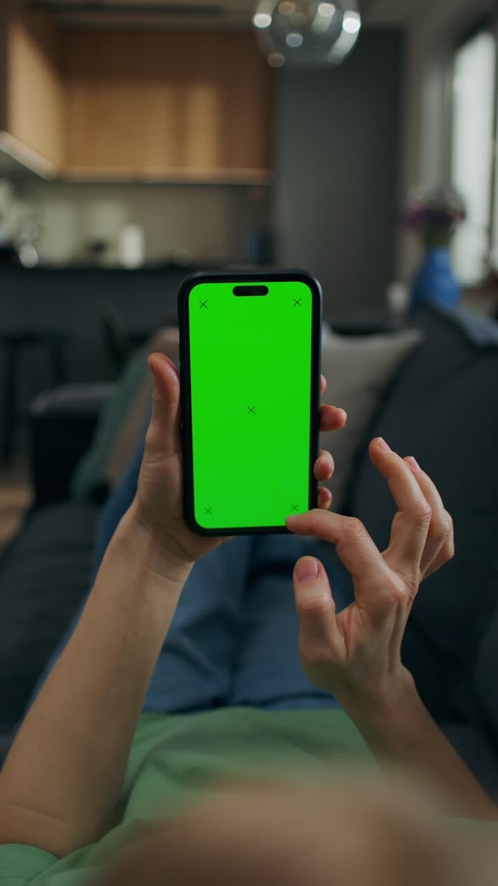 Woman using a smartphone with a green screen on a couch