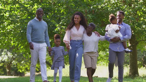 multi-generation family holding hands enjoying summer walk in countryside together