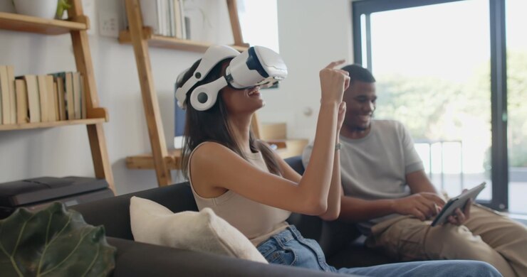 Coppia a casa, la donna che indossa un visore VR, gesticola per controllare la VR, l'uomo che tocca il tablet.