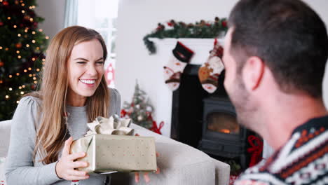 excited woman receiving christmas gift from man at home