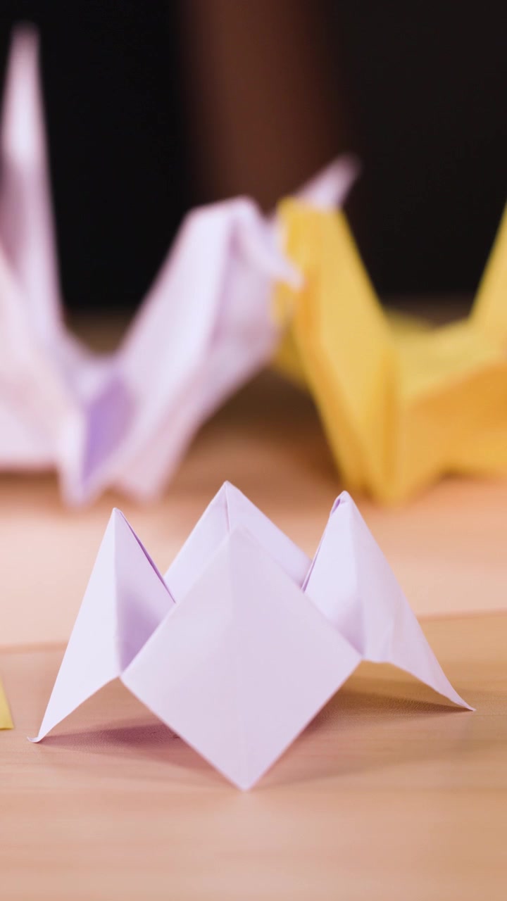 Et stillestående nærbillede viser hvide og gule papirorigamikraner på en træoverflade.