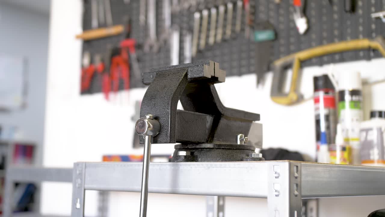 abrazadera de tornillo de banco giratoria de acero con yunque en un banco de trabajo con una variedad de herramientas en el tablero de clavijas detrás, cerca de la toma de movimiento