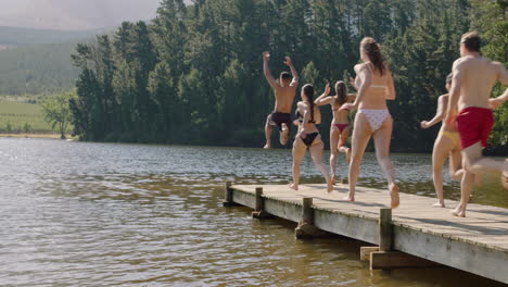 Grupo-De-Amigos-Saltando-Del-Embarcadero-En-El-Lago-Chapoteando-En-El-Agua-Disfrutando-De-La-Libertad-Divirtiéndose-Aventura-De-Verano-En-Vacaciones