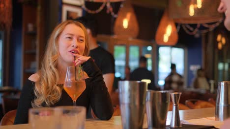 A joyful woman laughs heartily while savoring a delightful drink in a vibrant and lively restaurant atmosphere