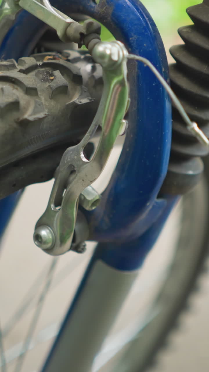 primer plano de alguien probando la funcionalidad del freno delantero de una bicicleta, el enfoque está en el neumático y el mecanismo del freno con un fondo borroso con marcas blancas