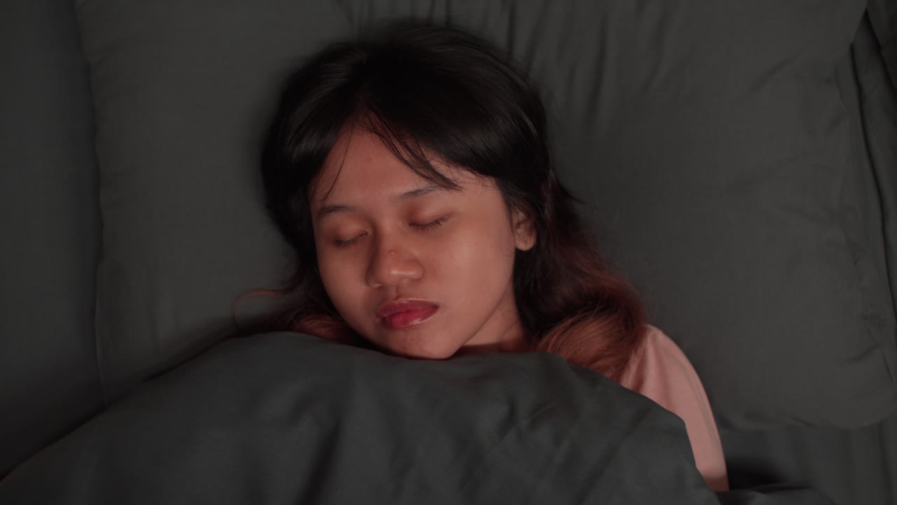 Sleeping woman, peaceful, calm expression, resting in cozy bed under gray blankets