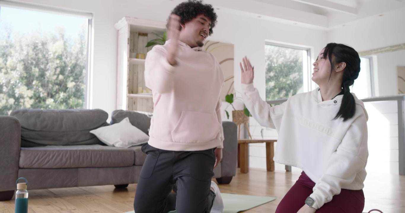 Diverse duo smiling, doing knee drives on mats, kneeling hand-slapping, stretching drinking bottles
