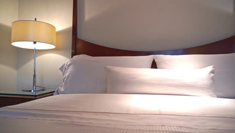 slow pan right on the made-up king-sized bed with white striped linen pillows and cover at night with turned on lamps in a hotel in houston, usa