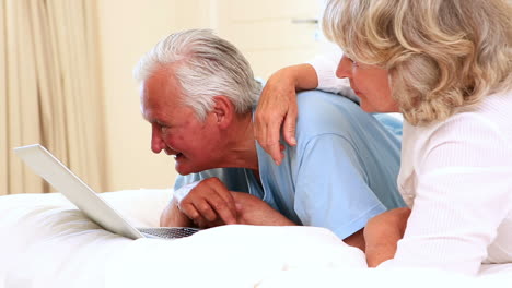 Senior-couple-lying-on-bed-using-laptop