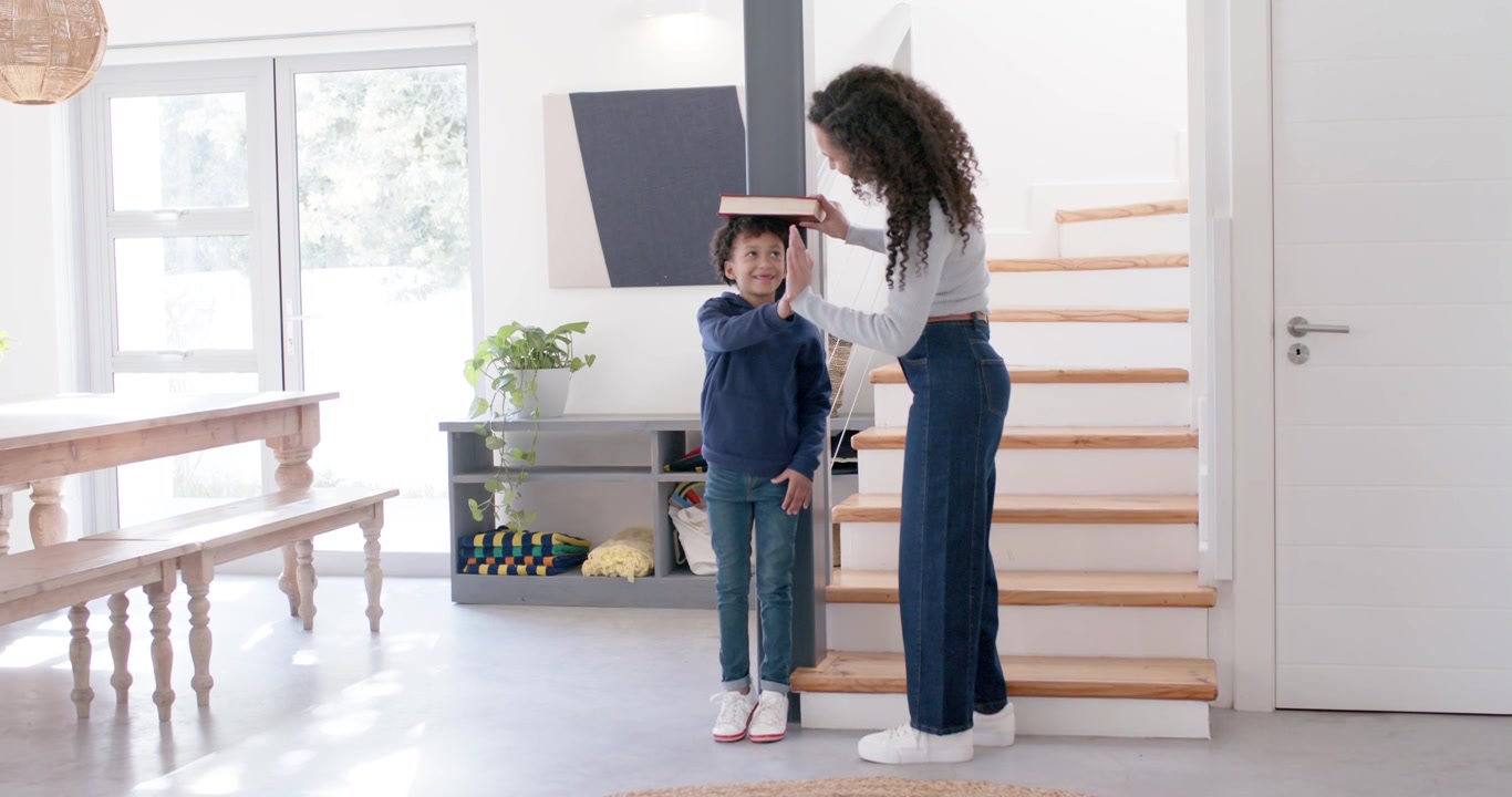 African American mother and child by post placing book on child's head at home, measuring height