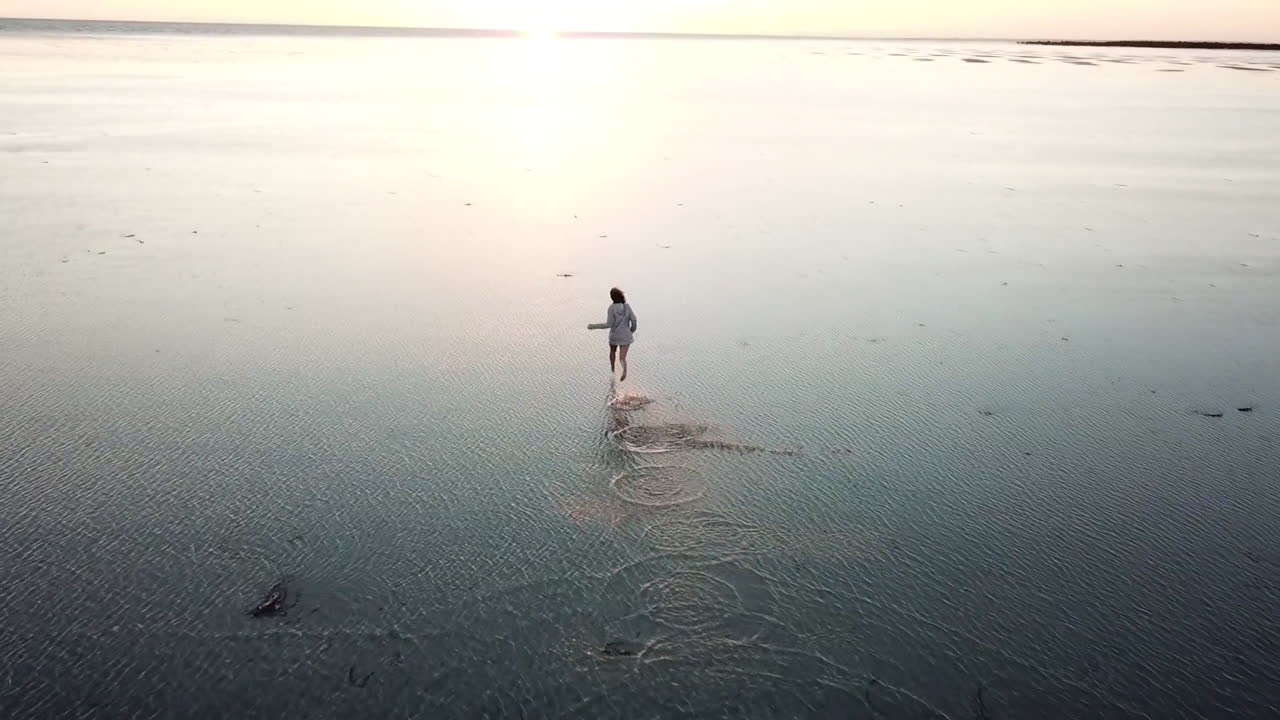 AERIAL SLOW MOTION - A teenage girl runs arms wide towards the sunset