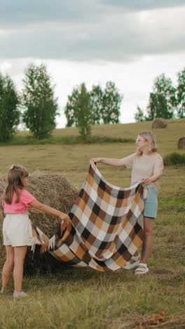 madre e hija extendieron una alfombra cerca de la bala de heno en una vasta tierra de cultivo, la abuela está junto con el niño, todos disfrutando de un momento rural pacífico juntos en un entorno rural abierto bajo un cielo despejado