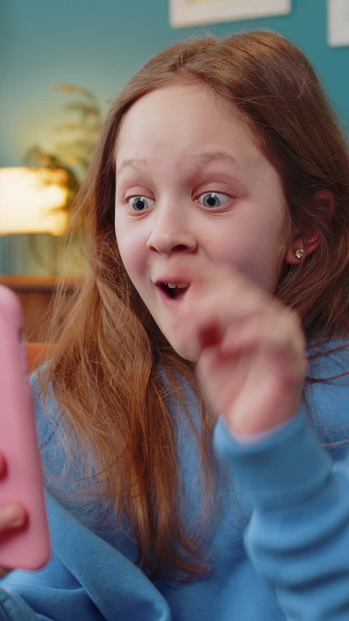 Happy child girl using smartphone playing game good positive news celebrate online win at home