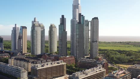 altos rascacielos se elevan por encima de la línea de árboles en buenos aires, con el vasto río de la plata en el fondo