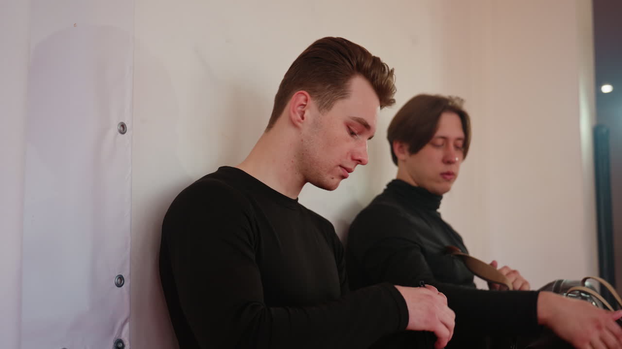 Young man in black uniform walk and sit on a bench indoors hand gripping clothing, expression calm yet thoughtful, moment reflecting silence, pause, discipline and readiness for action